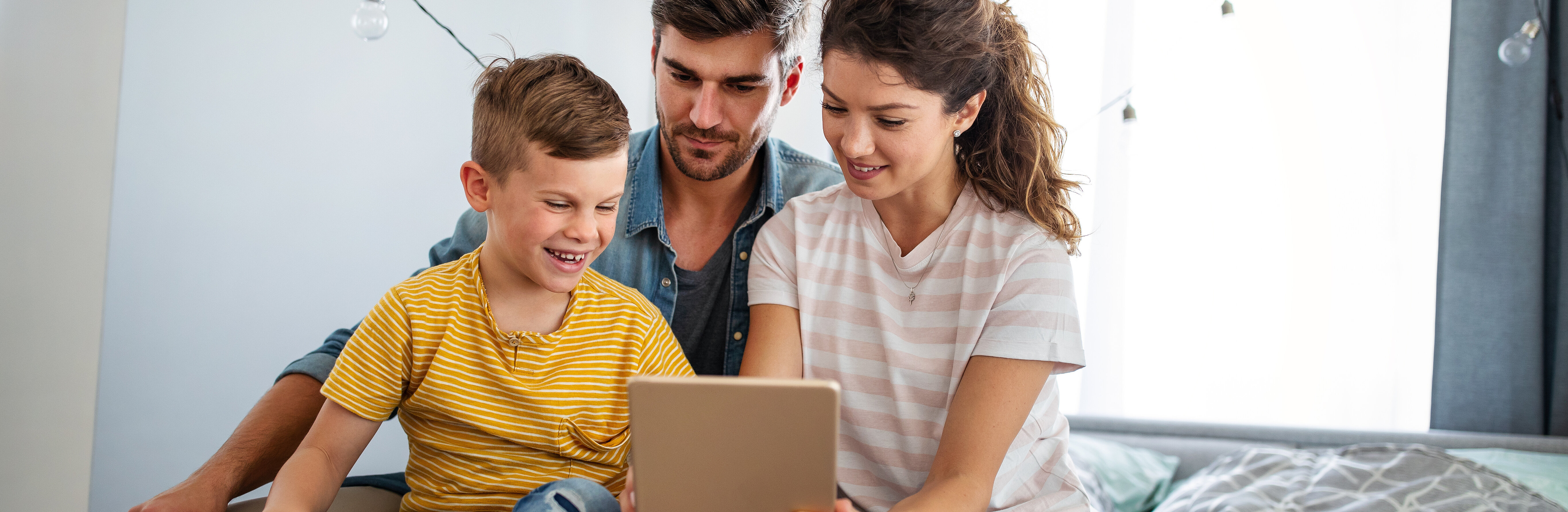 Familie sitzend auf dem Bett, betrachtet Tabletinhalt