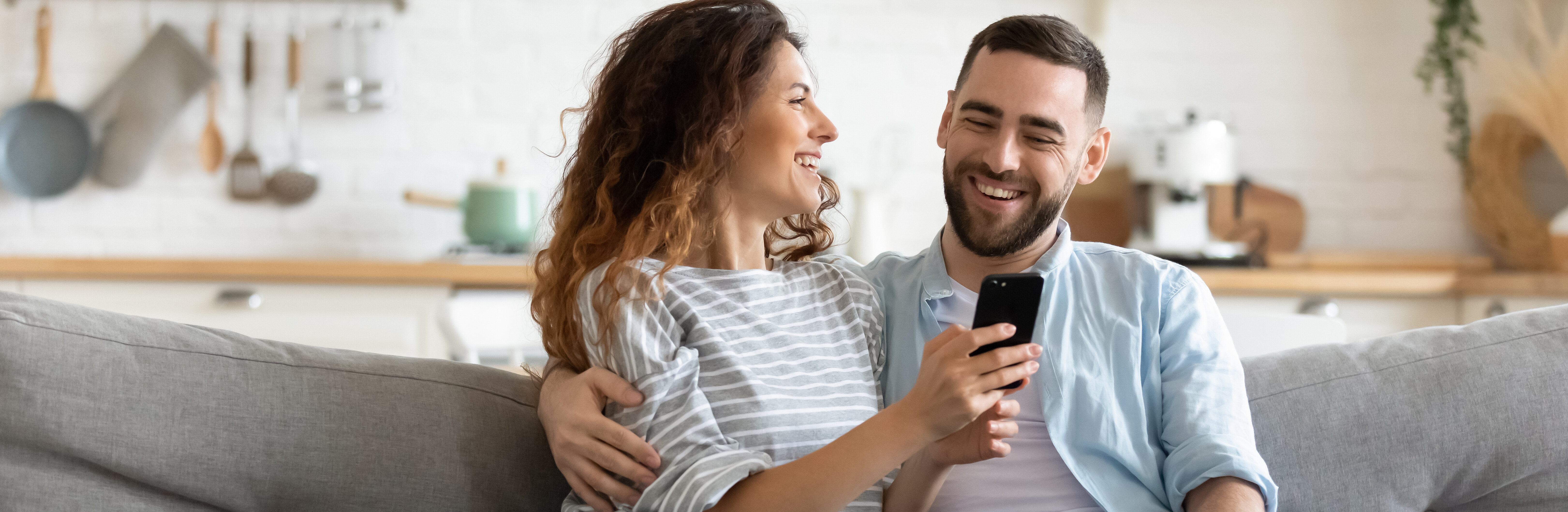 Paar auf dem Sofa sitzend, betrachtet lächelnd das Handy